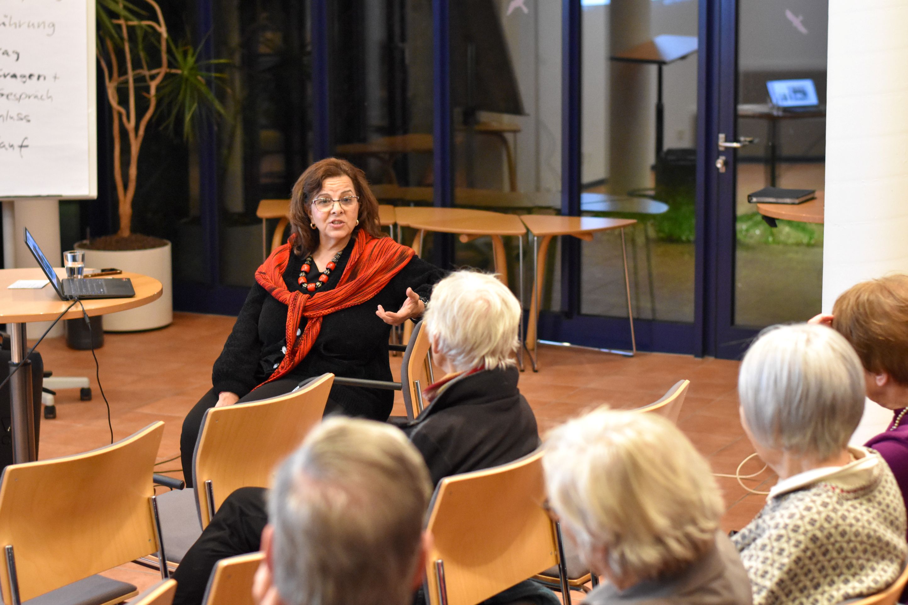 Eine Frau sitzt auf einem Stuhl und spricht vor einem Publikum.