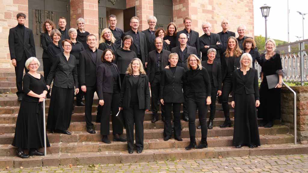 Kammerchor_Cantemus_Bensheim_C_Armin_Falb_16zu9.jpg Gruppenfoto des Kammerchors Cantemus Bensheim. Die Sängerinnen und Sänger stehen in schwarzer Konzertkleidung in mehreren Reihen auf einer breiten Steintreppe vor dem Eingangsportal einer Kirche.