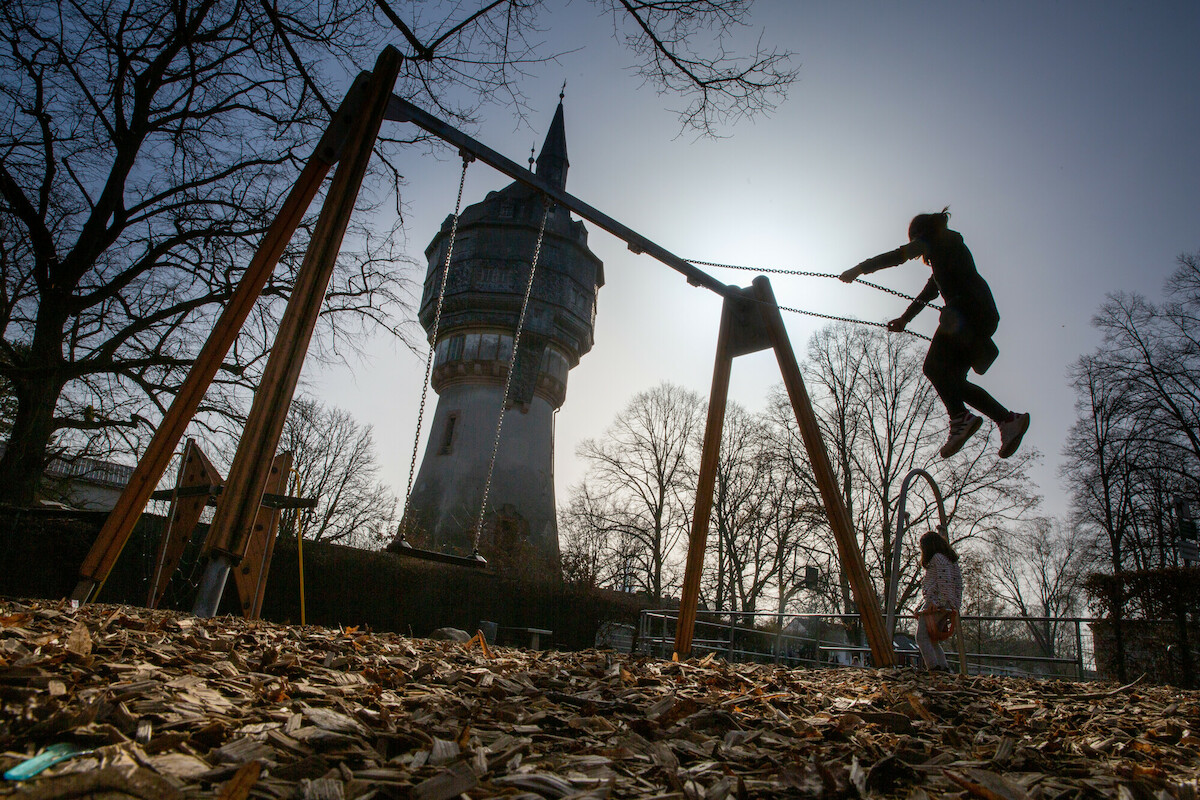 Kind schaukelt auf Spielplatz, im Hintergrund eine der Frankfurter Warten.