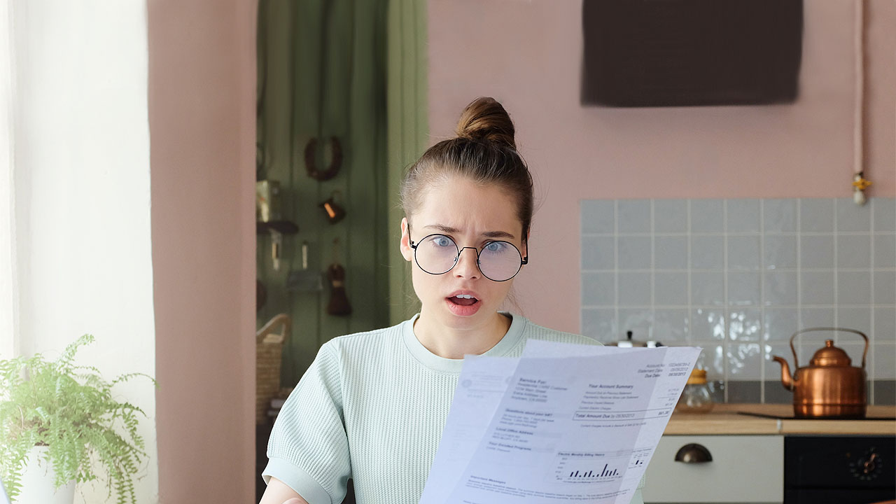 Frau mit High Bun schaut entsetzt auf ein Papier und ihr Smartphone