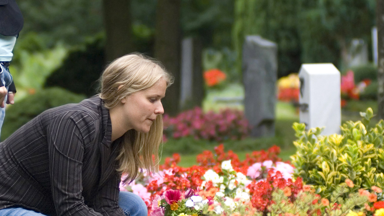 Eine junge Frau an einem Grab mit Blumen