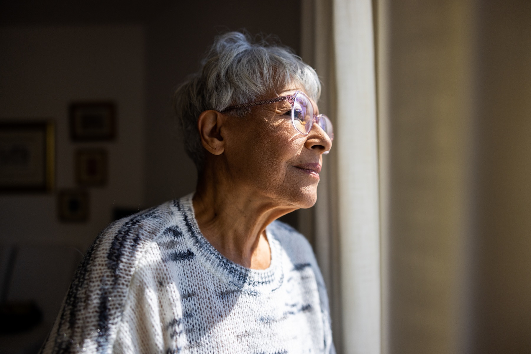 Eine alte Frau schaut wehmütig nach draußen durch ein Fenster. Sie ist einsam.