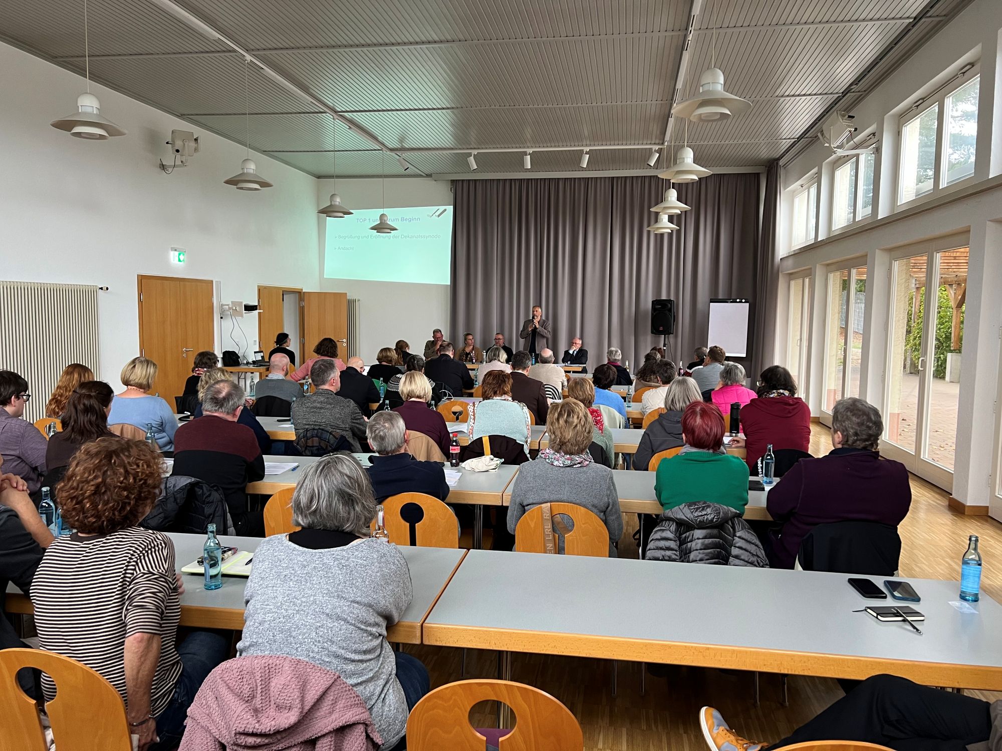 viele Menschen sitzen in einem großen Raum und schauen nach vorne Richtung Bühne