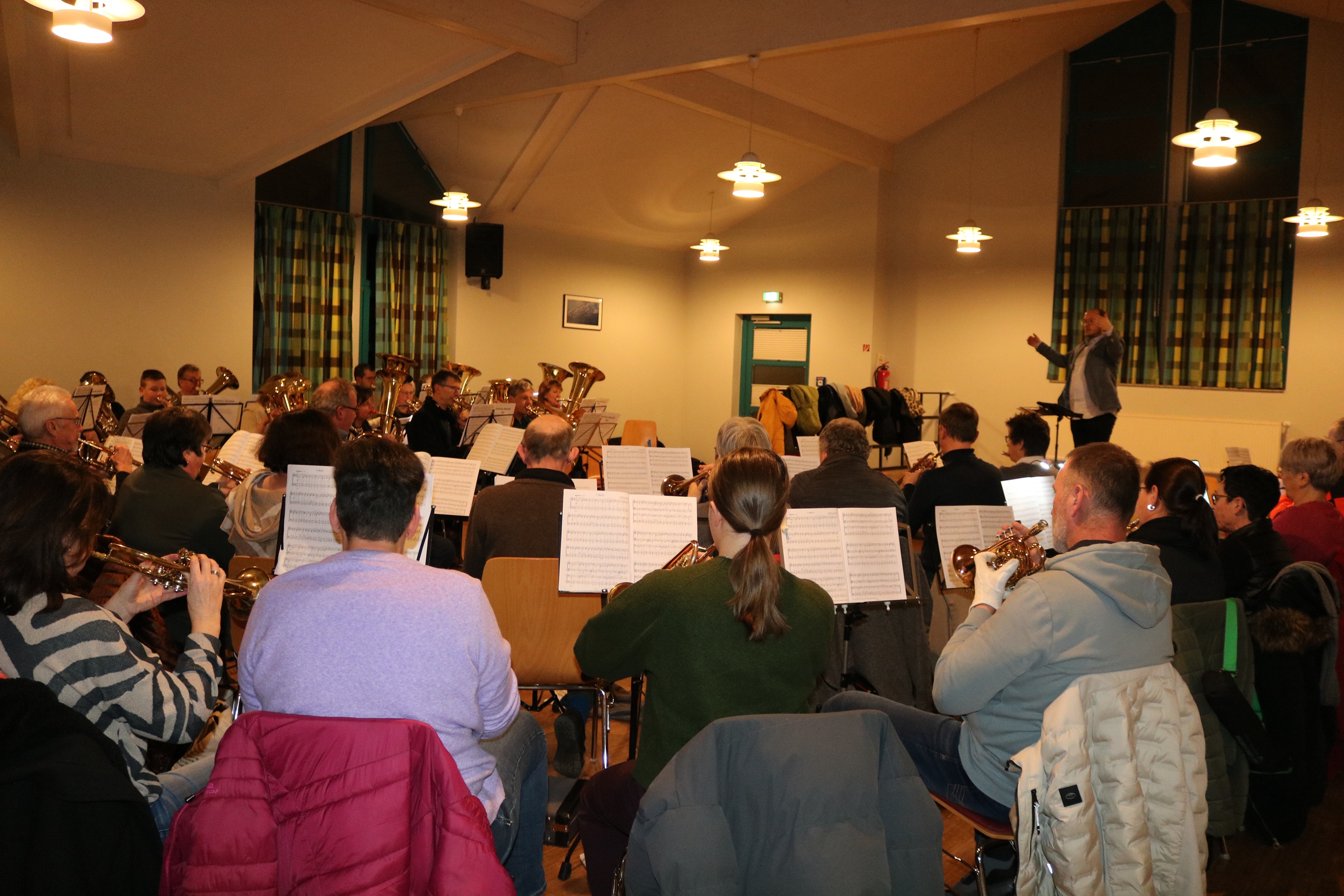 Viele Posaunenchorbläser in einem Raum, mit dabei ist ein Dirigent.