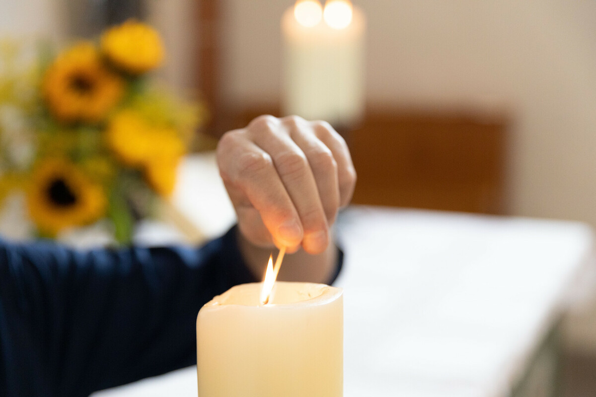 Eine Hand hält zwischen Schere und Fingern einen Ring aus Wachs, welcher von der sich darunter befindenden Kerze abgeschnitten wurde.