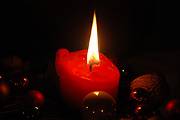 Kerze und Weihnachtskugeln vor dunklem Hintergrund