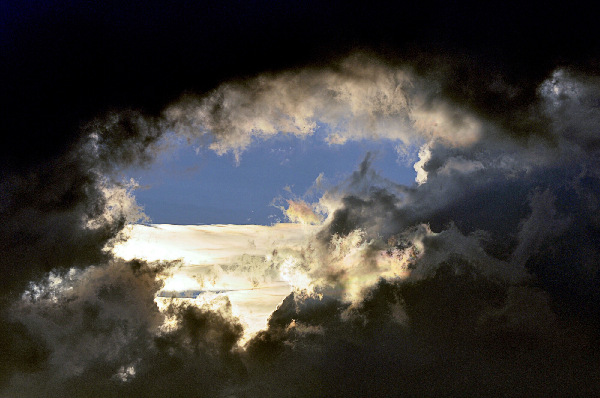 Blick durch ein dunkles Wolkenloch in einen blauen Himmel