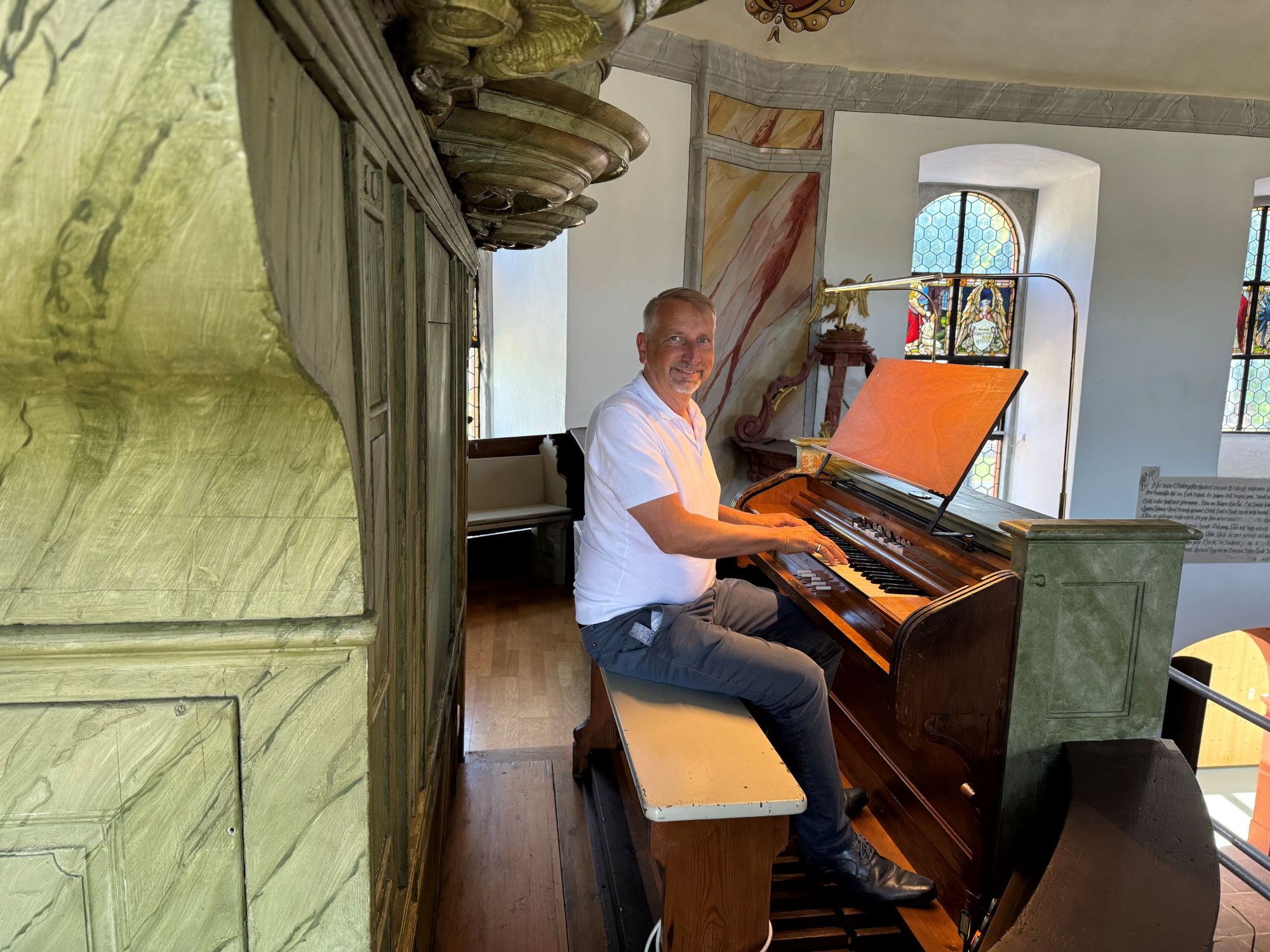 Ein Mann sitzt am Spieltisch einer Orgel. Ringsumher ist ein Teil des Inneren einer barock gestalteten Kirche erkennbar