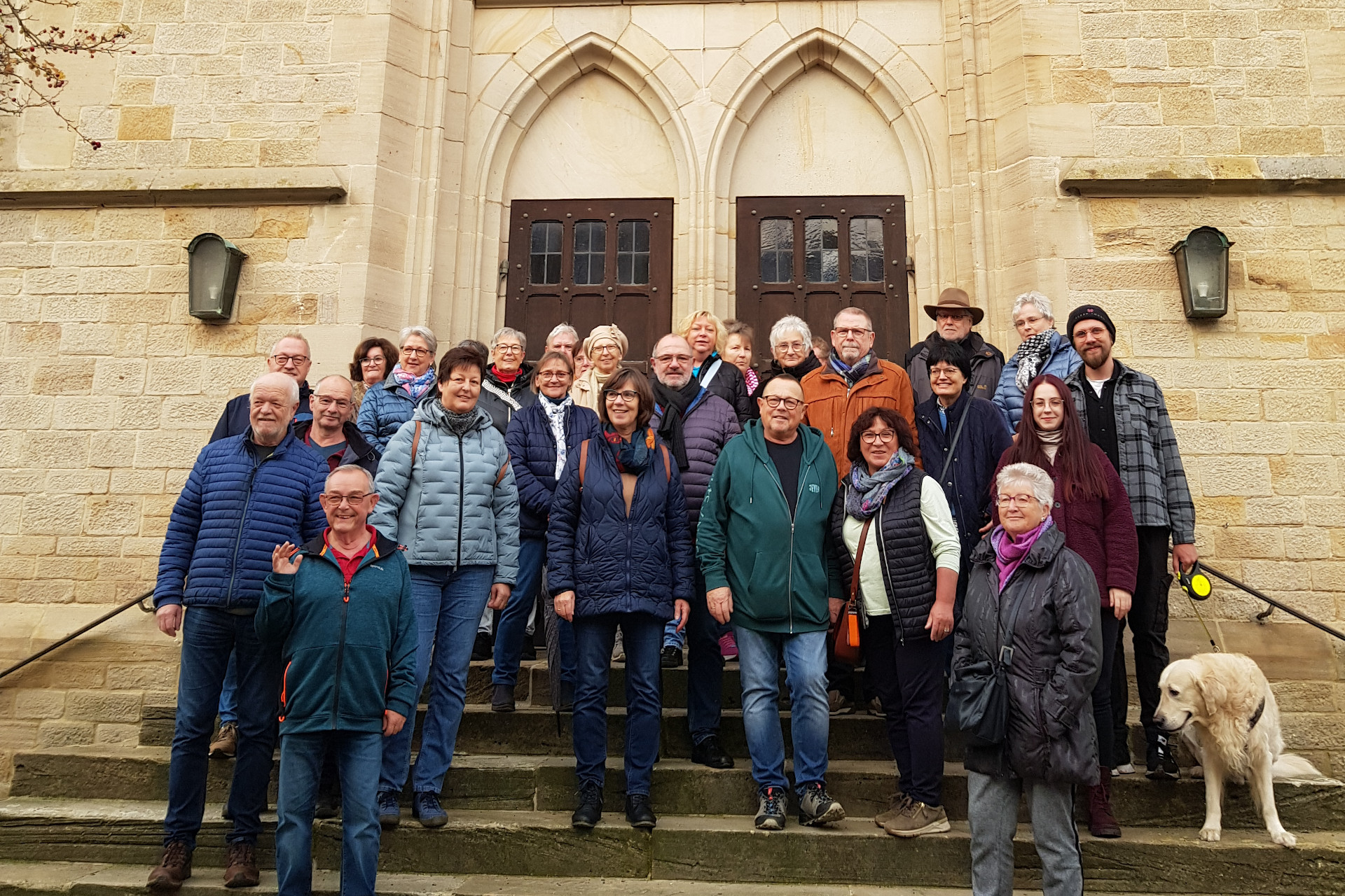 Eine Gruppe aus jungen und alten Menschen steht auf einer Treppe vor einer Kirche.