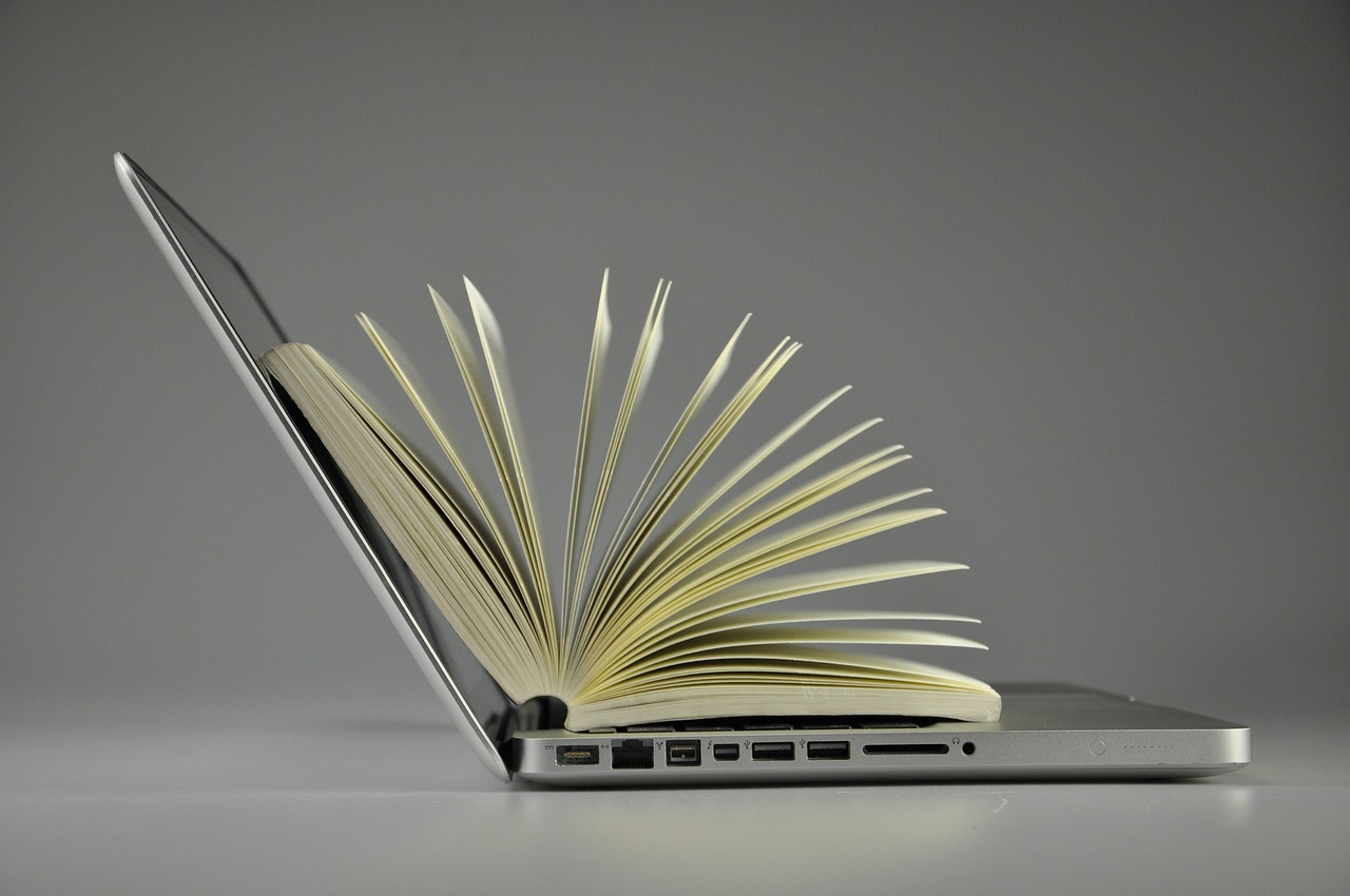 Aufgeschlagenes Buch liegt auf aufgeklapptem Laptop