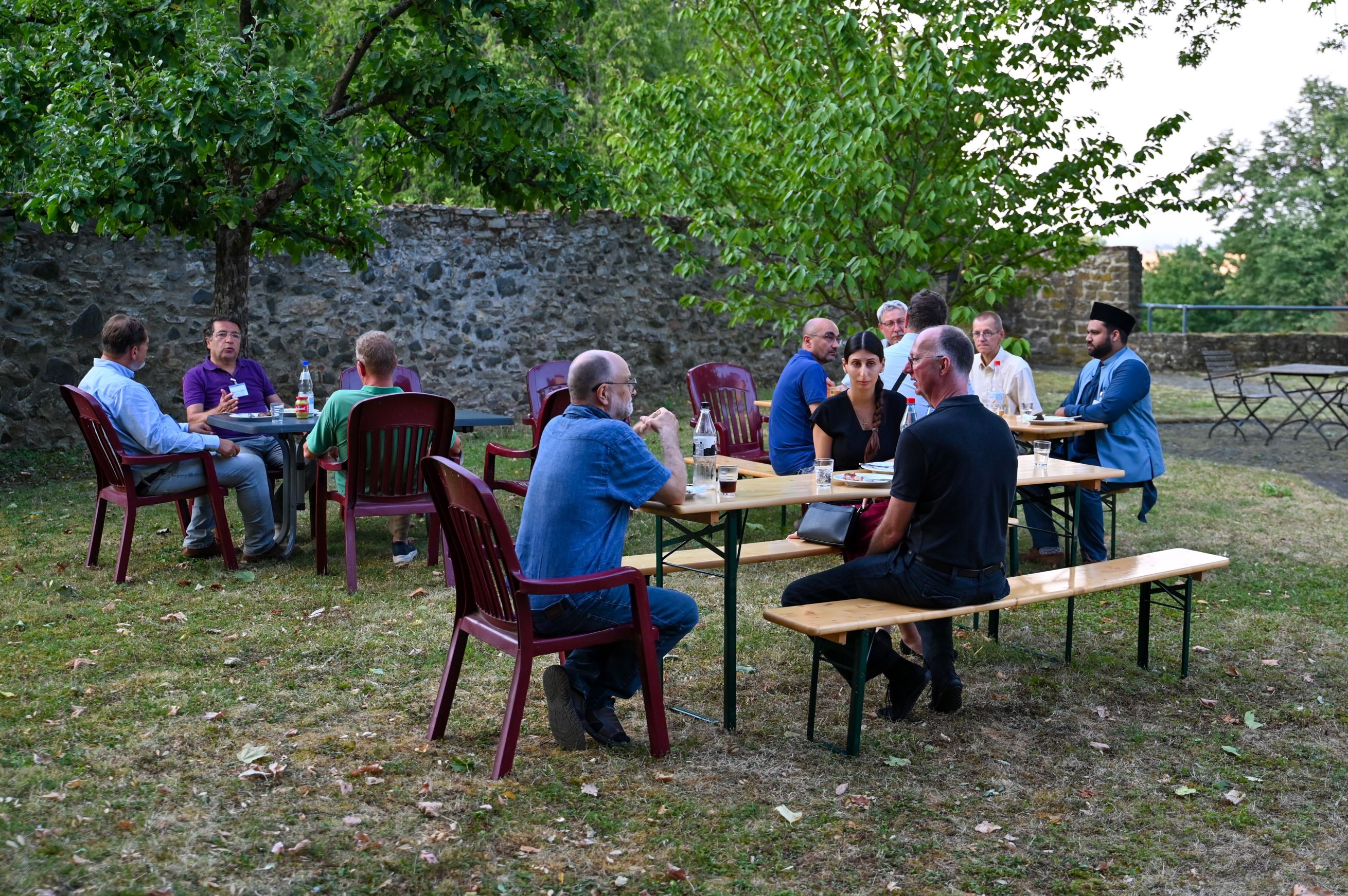 Eine Gruppe von Menschen sitzt an Bierzeltgarnituren und Tischen im Garten des Evangelischen Dekanats Wetterau.