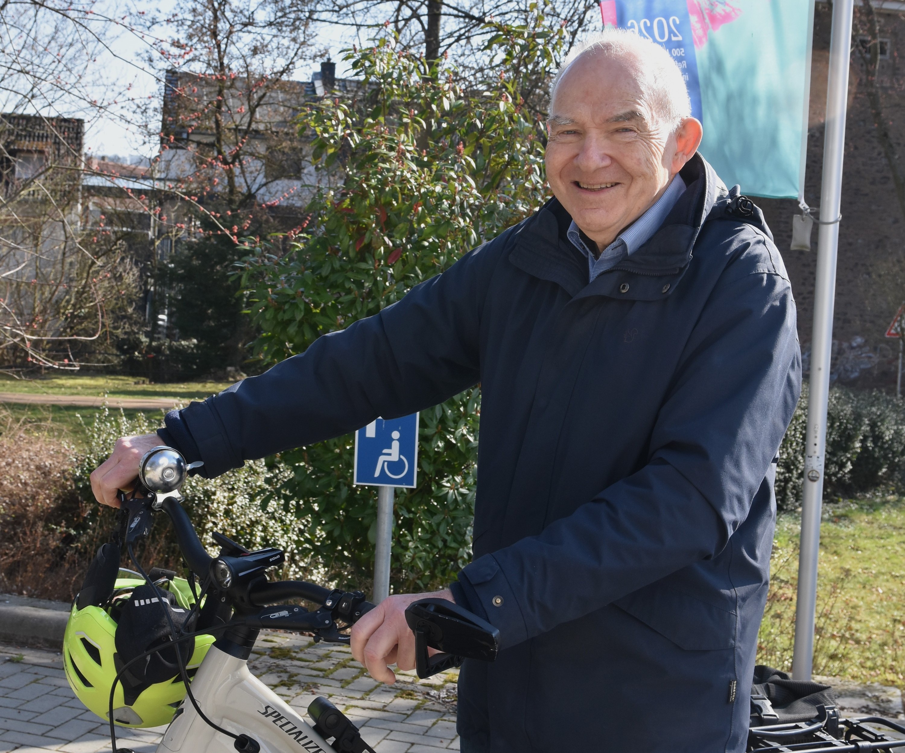 Rolf Hartmann, schütteres graues Haar, dunkler Anorak, stehend mit seinem hellen Fahrrad, beide Hände am Lenker, daran hängt ein grüner Fahrradhelm