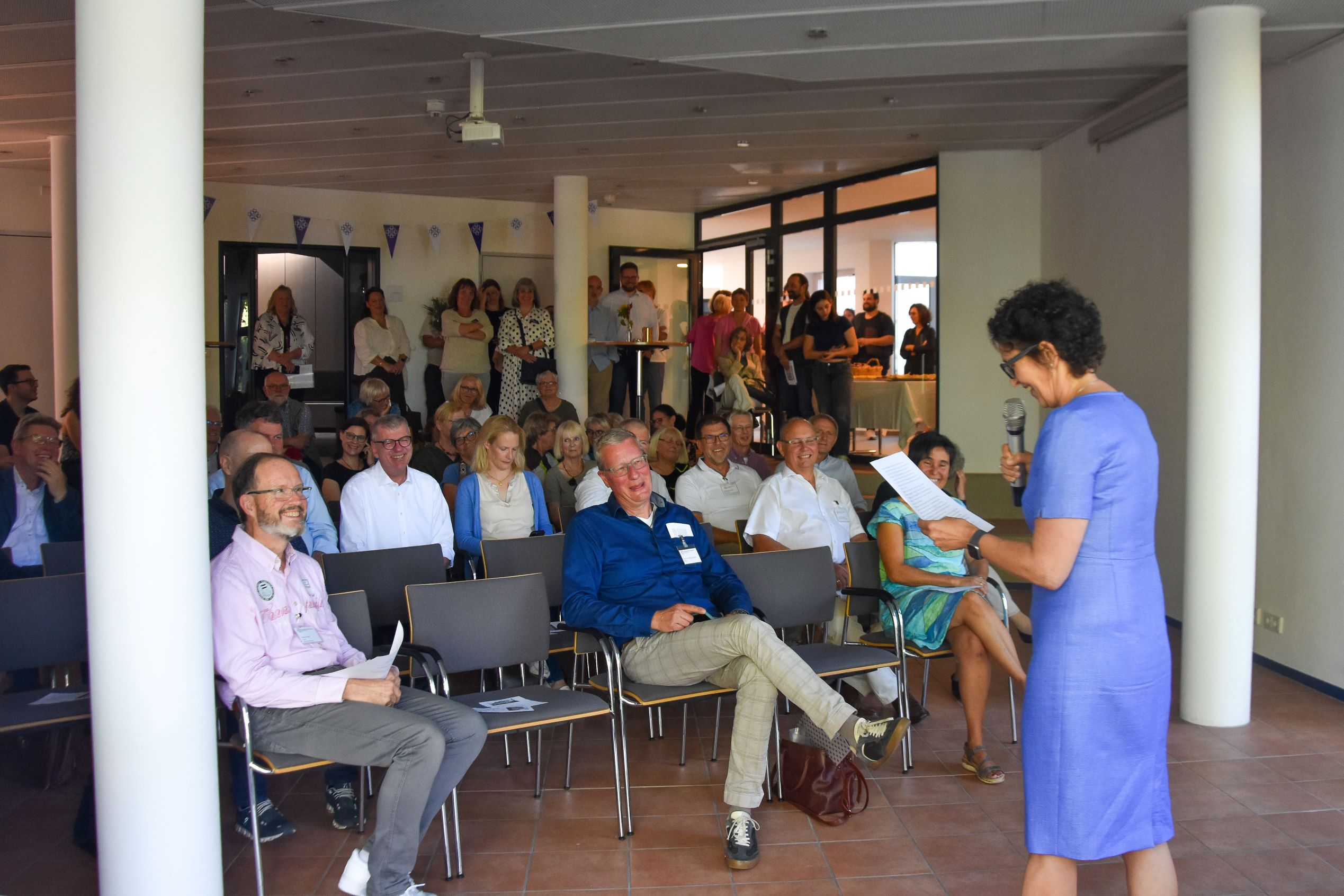 Eine Frau spricht vor einer versammelten Menge im Forum des Haus Friedberg.
