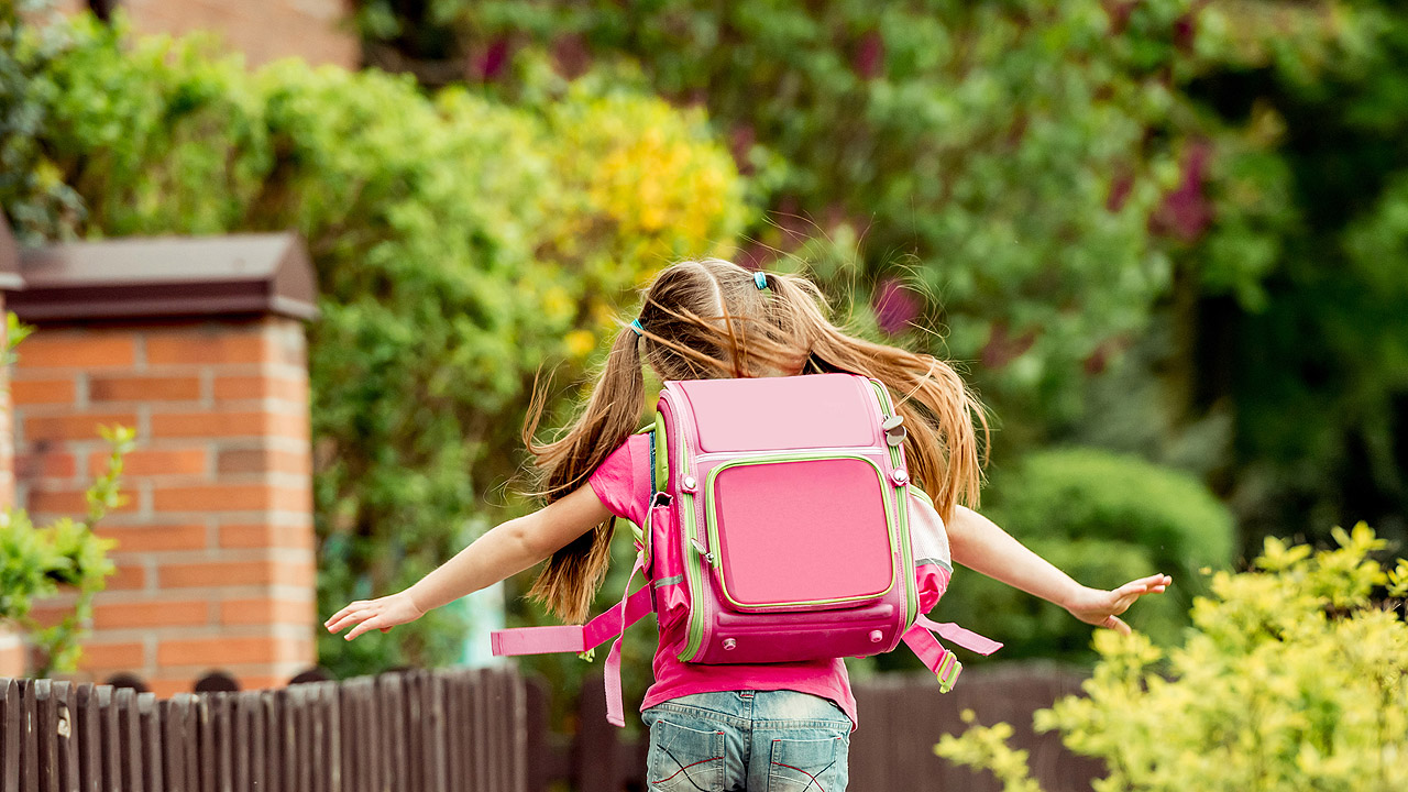 Mädchen mit rosa Schulranzen rennt zur Schule