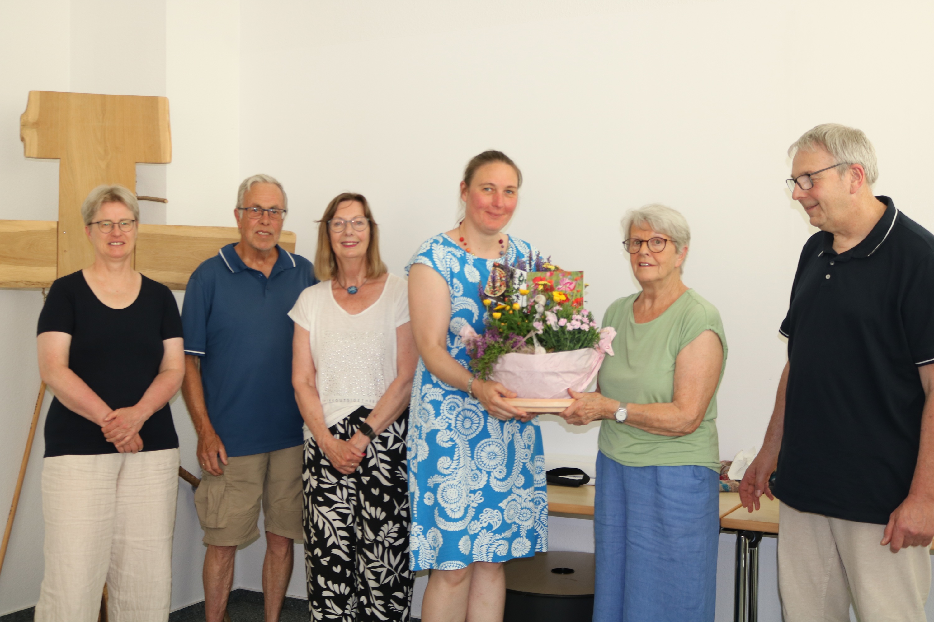 Gruppe von Menschen vor einem Kreuz, eine bekommt einen Blumenstrauß