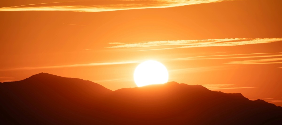 Feurige Sonne geht hinter Bergrücken auf