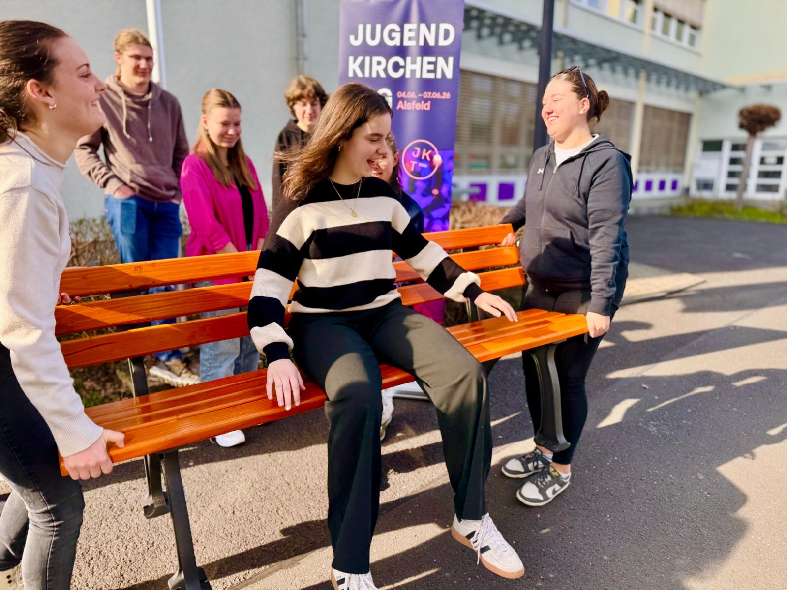 Jugendliche tragen eine Bank und strahlen um die Wette