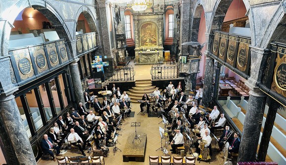 Etwa 60 Blechbläser sitzen im Kirchraum der Unionskirche Idstein. Von der Empore aus fotografiert sieht man auch den Altarraum.