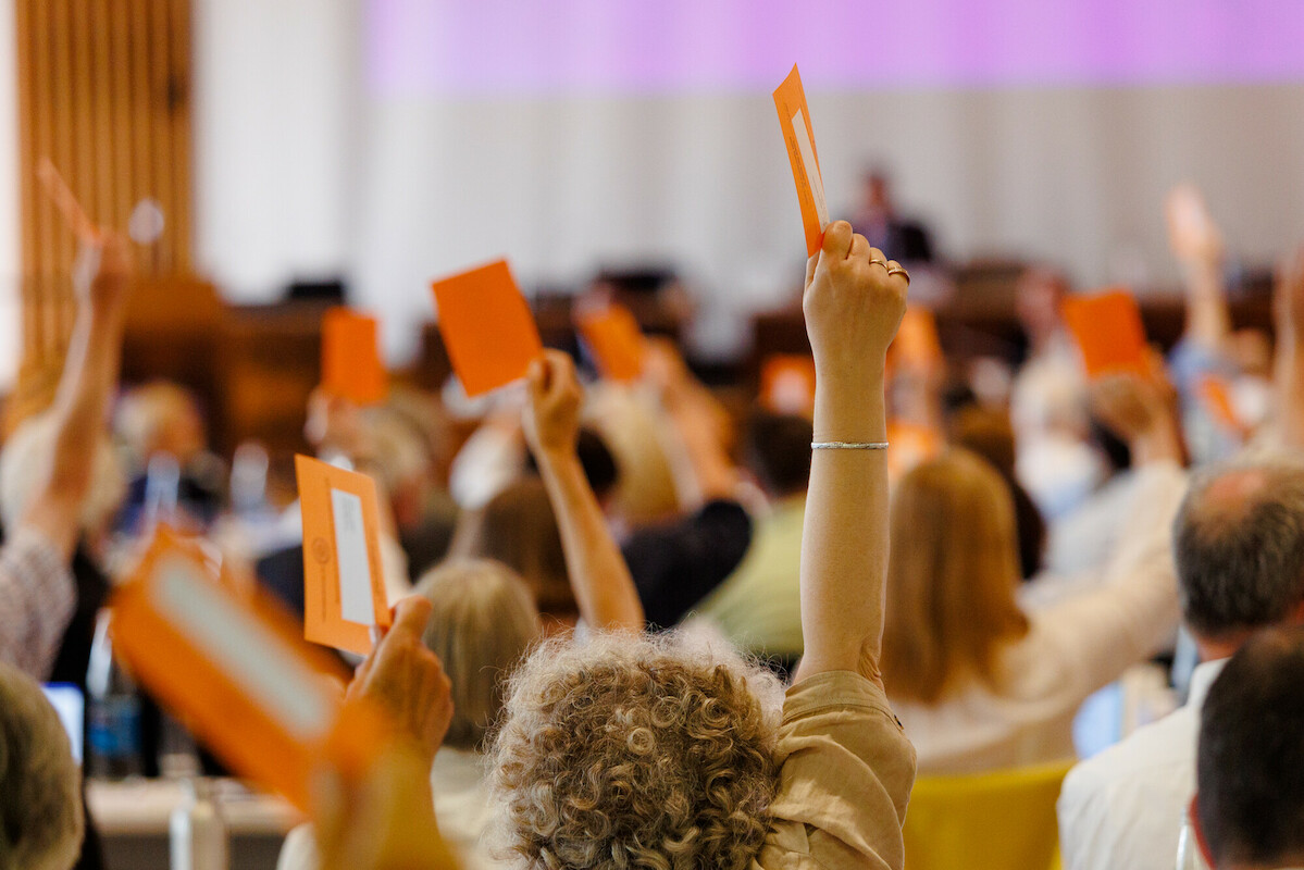 Man sieht auf Hände, die einen orangenen Abstimmzettel halten