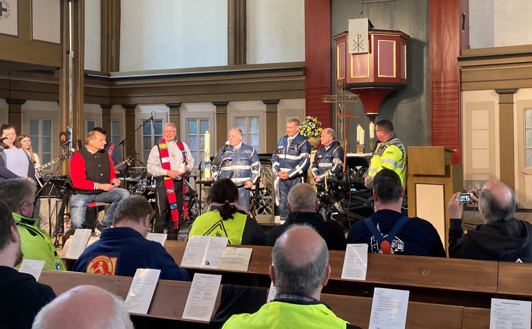 Vor dem Altar steht ein Pfarrer mit Stola und mehrere Polizisten in ihrer Uniform für das Motorrad 