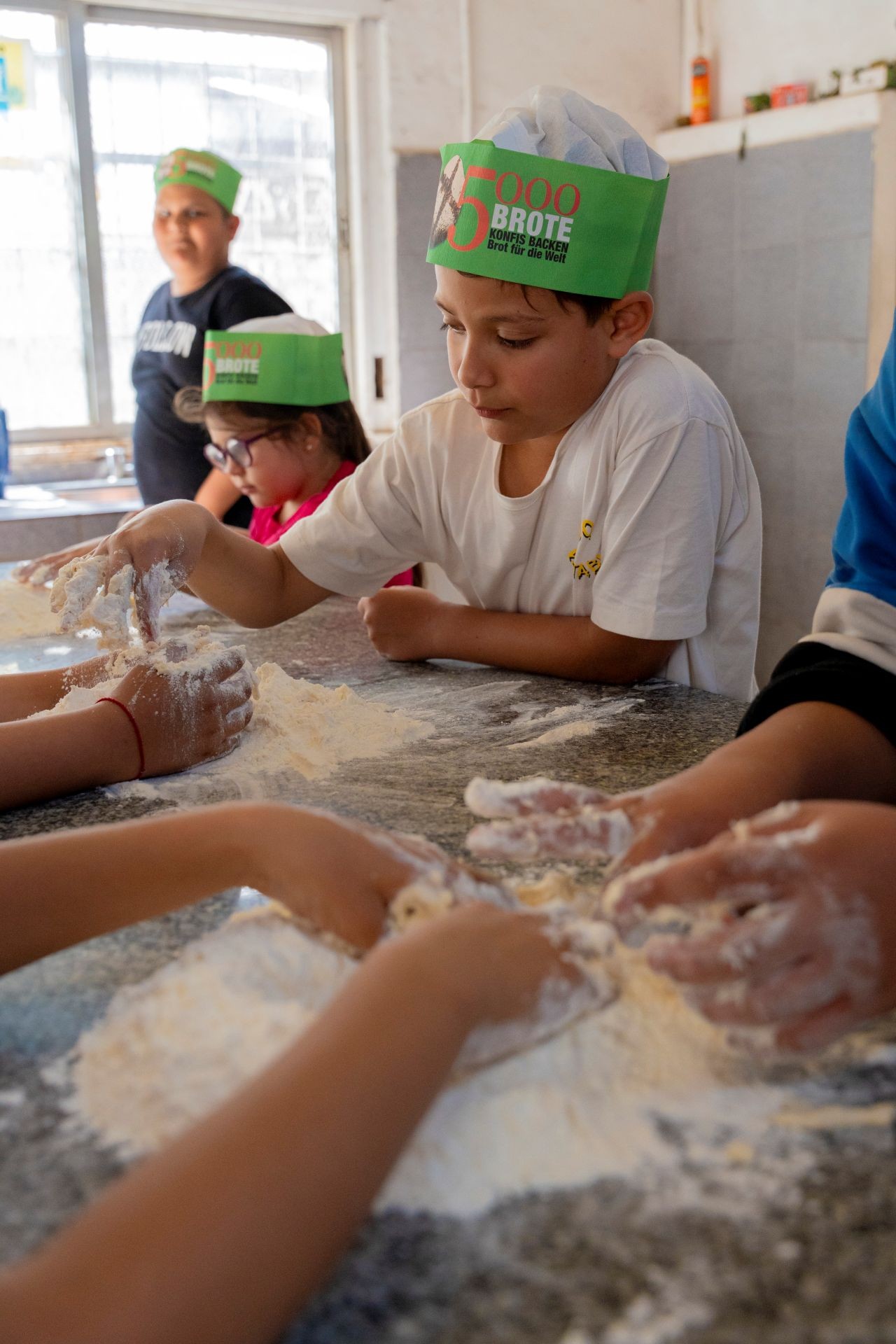 Kinder sitzen an einem bemehlten Tisch und backen Brot
