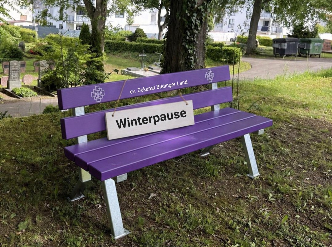 Das Bild zeigt die lilafarbene Trauerbank auf dem Friedhof in Nidda, im Hintergrund sieht man Baumstämme. Die Bank trägt die Aufschrift Dekanat Büdinger Land. Auf der Bank steht ein Schild mit der Aufschrift "Winterpause", dieses Schild wurde mit KI generiert.