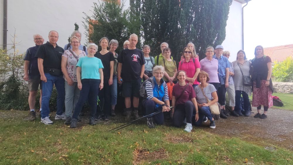 Gruppe von Frauen und Männern vor einem hohen Busch und einer Kirchenmauer