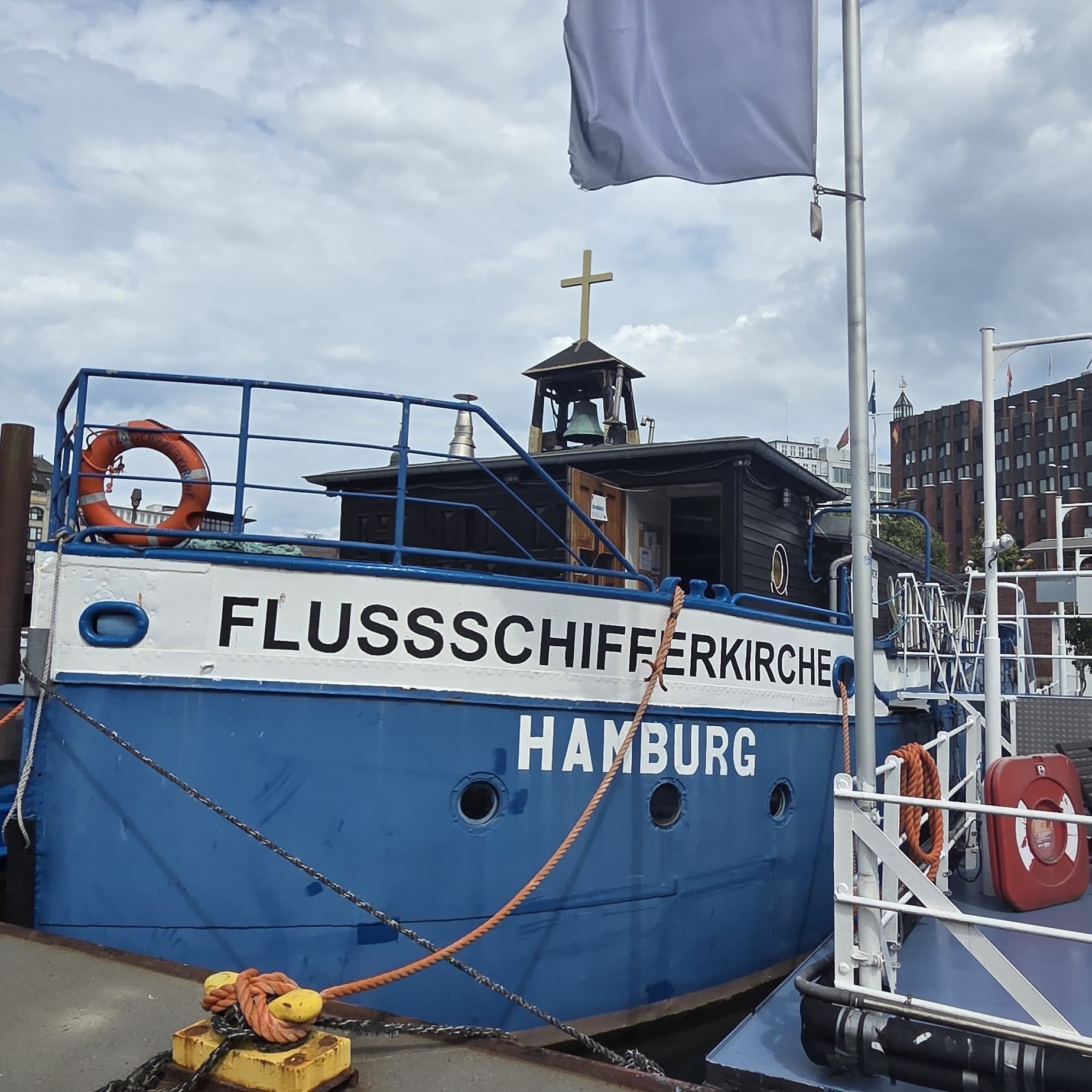 Blau-weißes Schiff mit der Aufschrift "Flussschifferkirche Hamburg" und Rettungsring an der Reling.