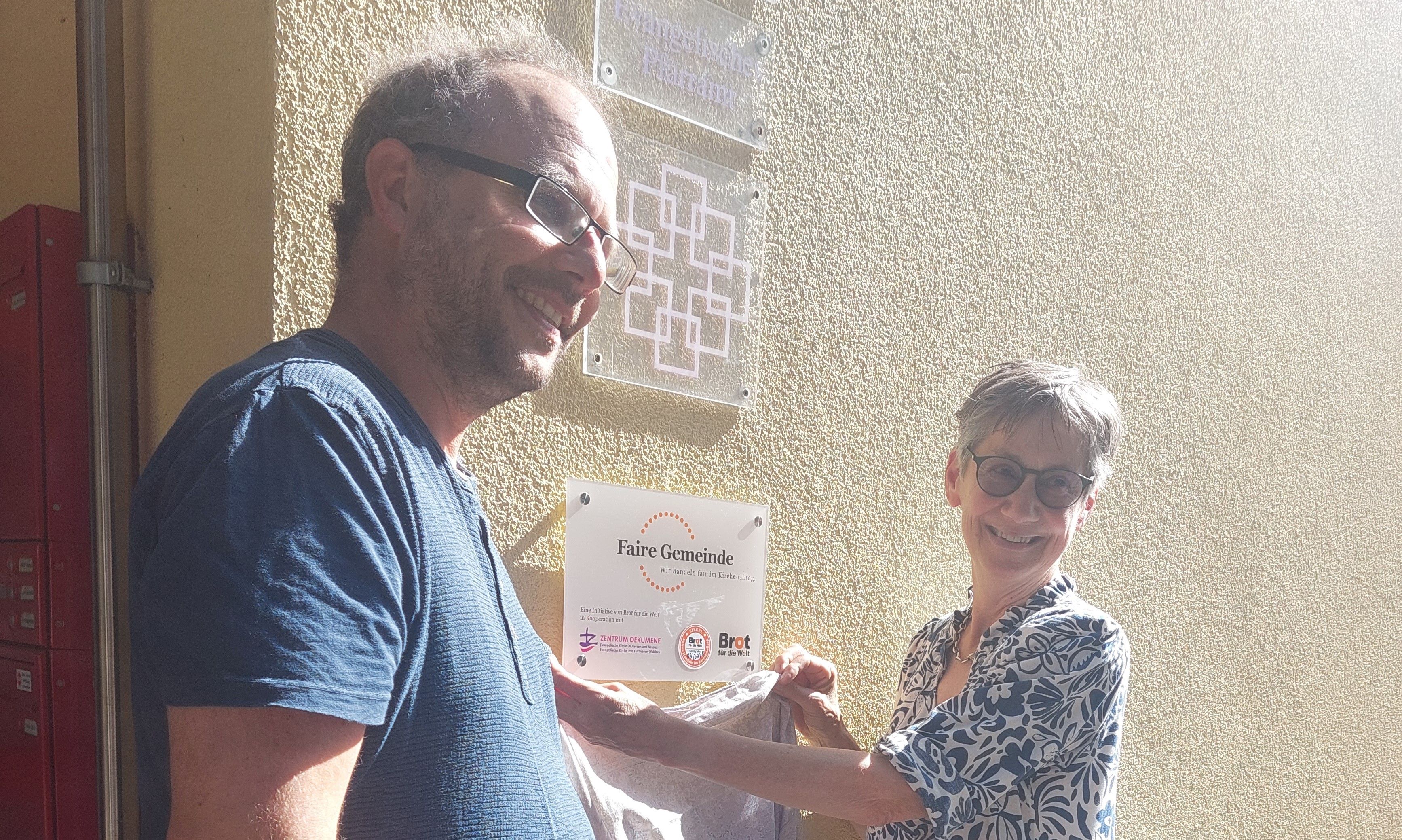 Pfarrer Christian Albers und Dr. Beate Schaupp vor der Plakette "Faire Gemeinde"