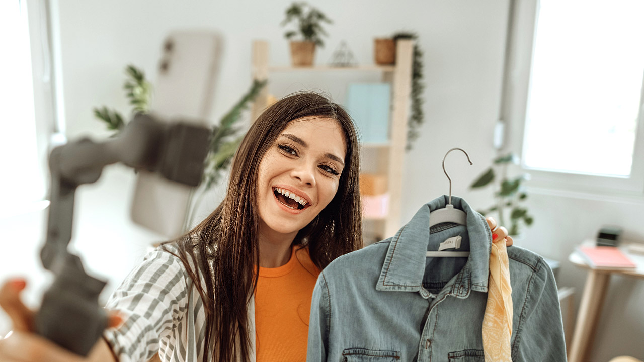 Eine junge Frau hält ein dunkles Jeans-Männerhemd in der Hand und macht von der Szene ein Selfie