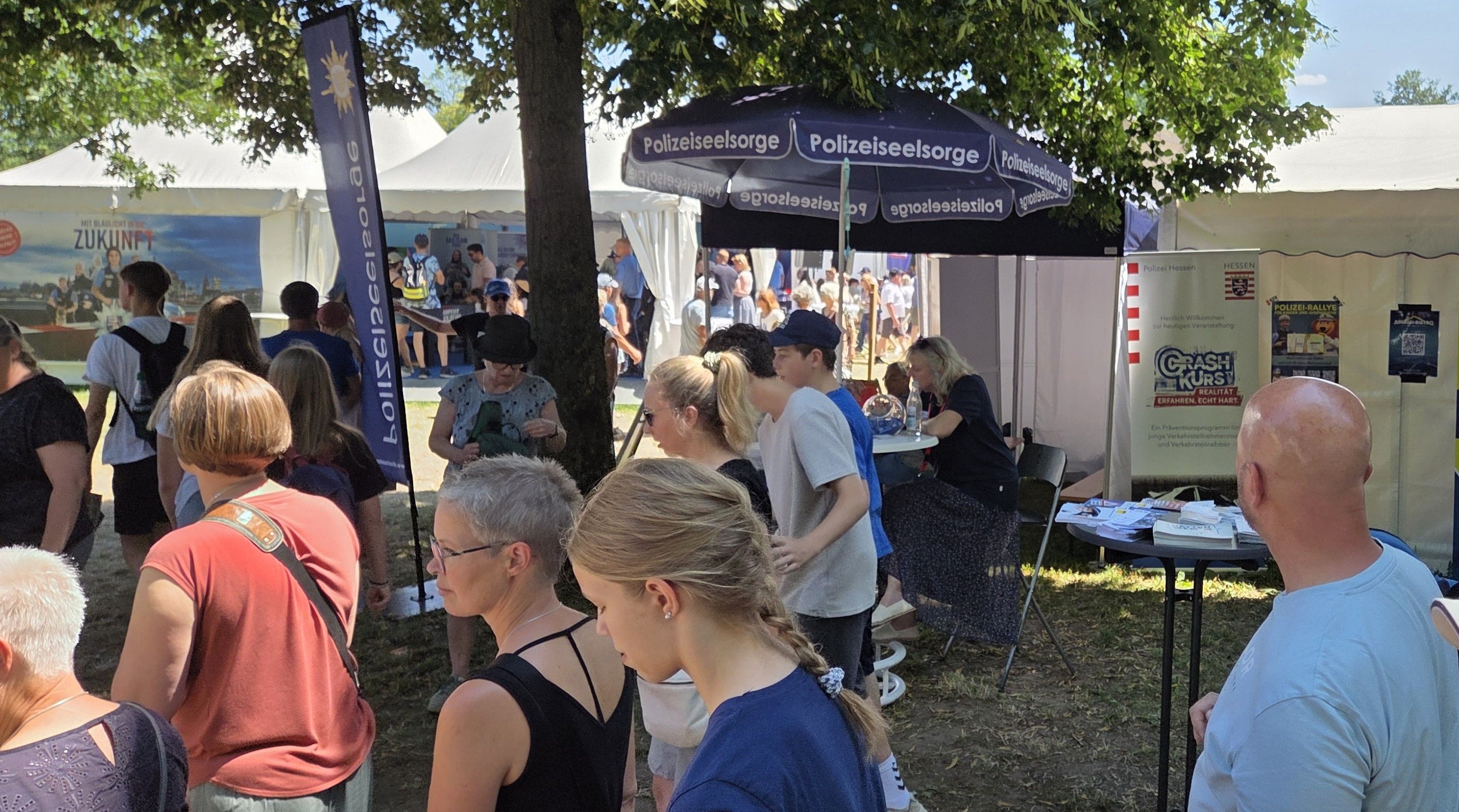 Viele Menschen sind unterwegs. Im Hintergrund ist ein Sonnenschirm der Polizeiseelsorge zu sehen.
