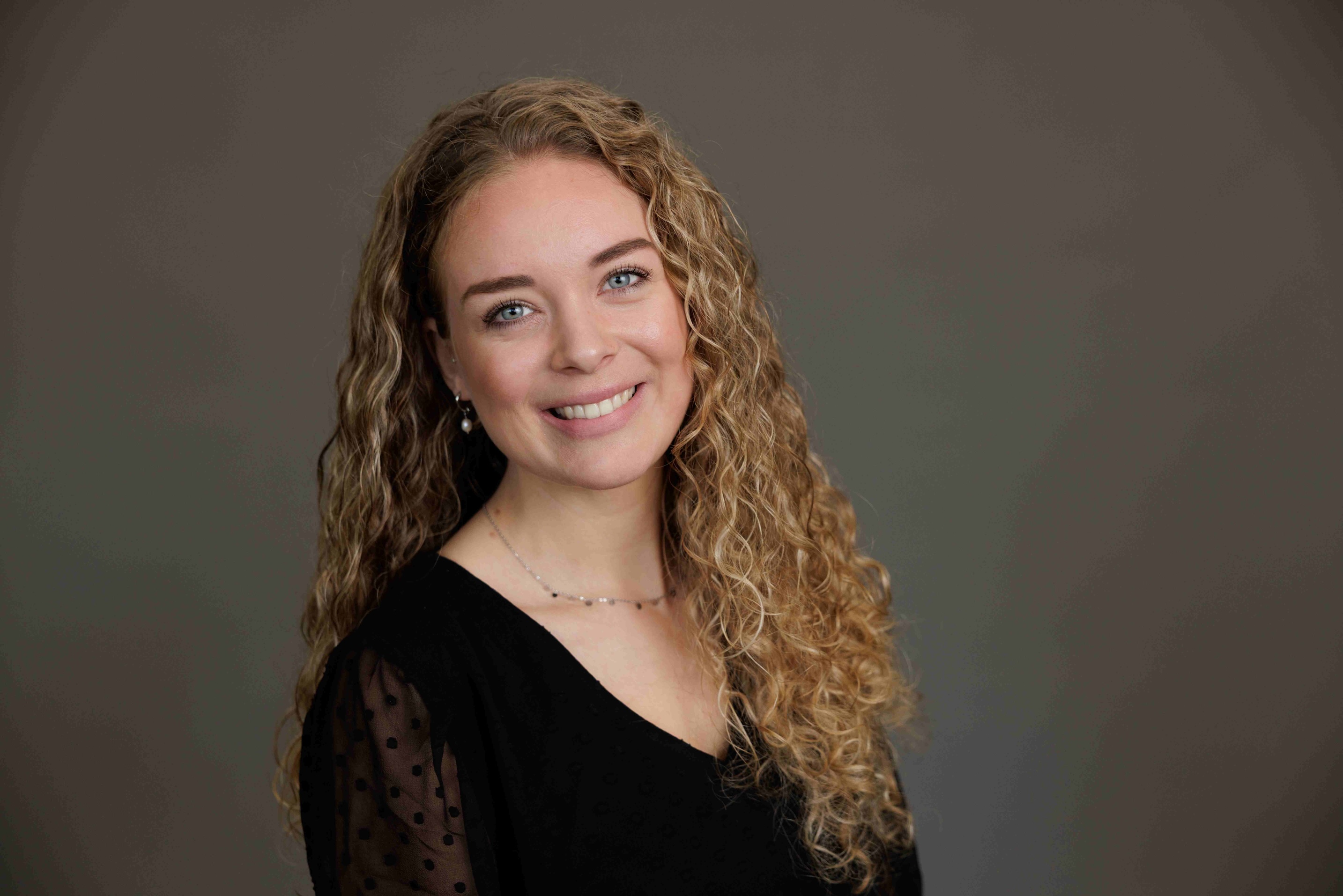 Das Bild zeigt eine junge Frau mit langen, gelockten, blonden Haaren, die in die Kamera lacht