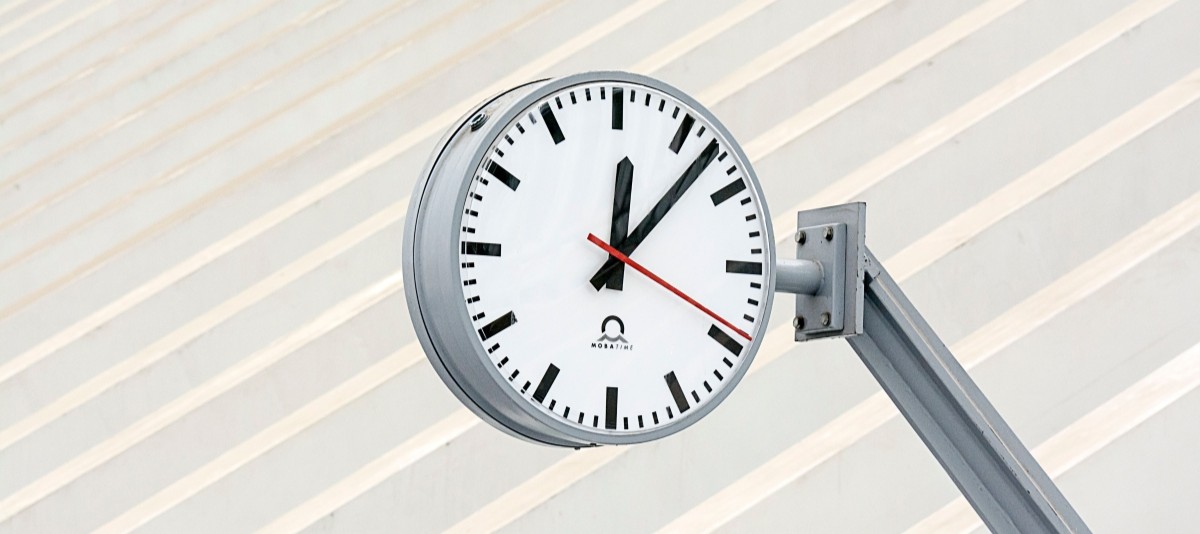 Nahaufnahme einer modernen Uhr mit minimalistischem Design vor einem gestreiften Hintergrund.