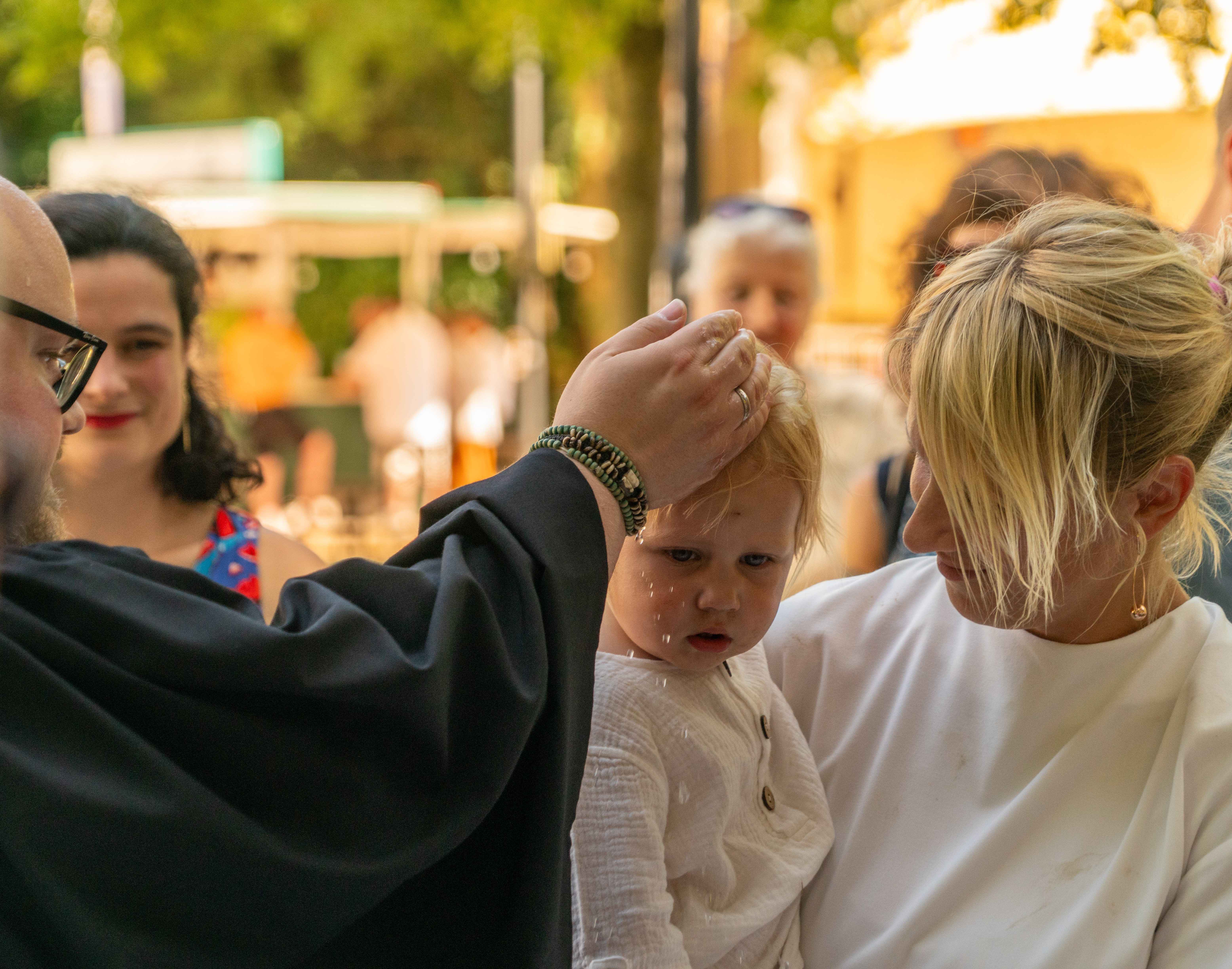 Vikar Christian Ulrich aus Niederhöchstadt bei der Taufe eines kleine Mädchens, das getuft wird sowie deren Mutter und Patentante.