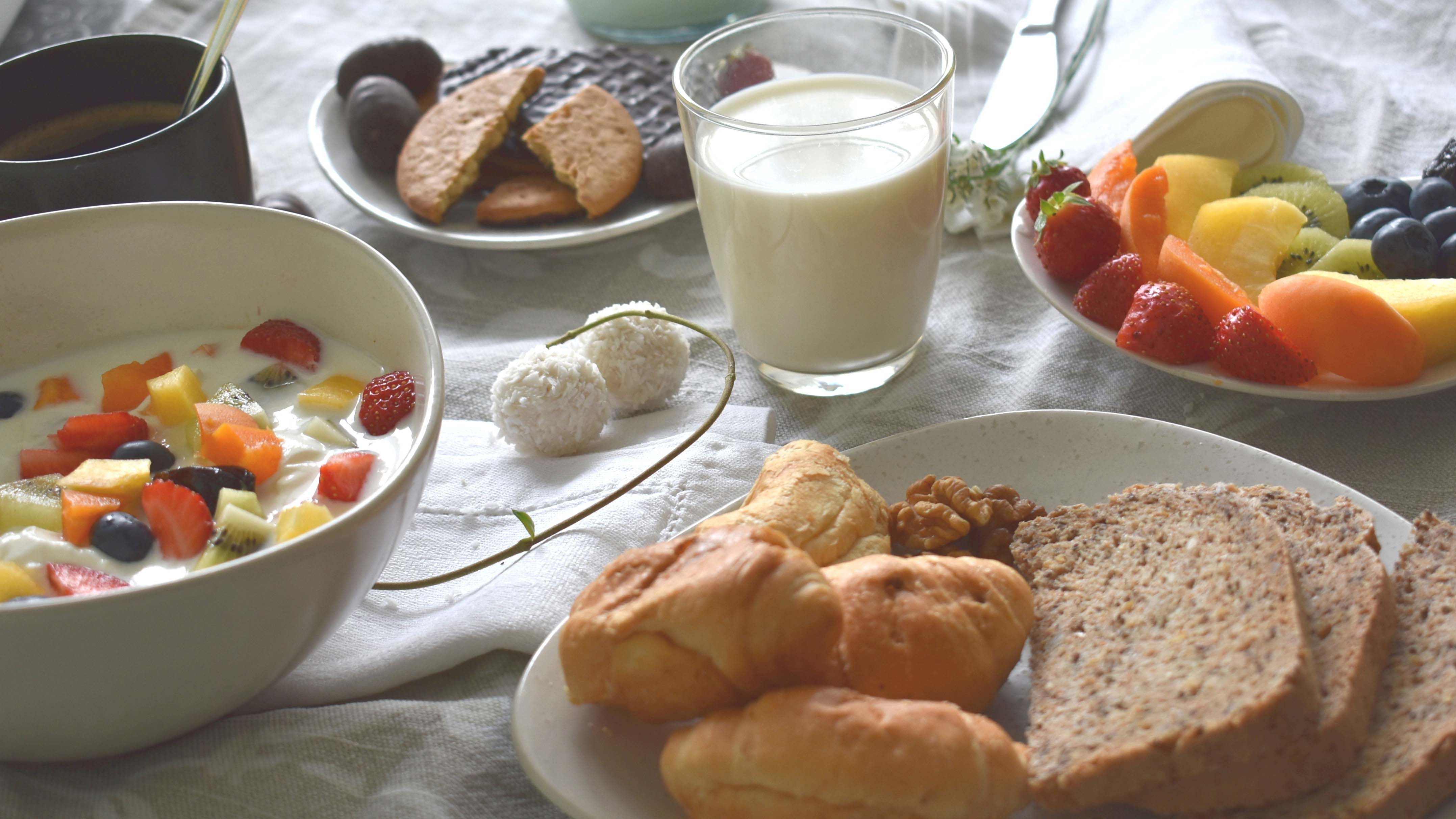 Frühstück mit Joghurt und frischem Obst, Milch, Gebäck, Brot und Keksen auf einem gedeckten Tisch.