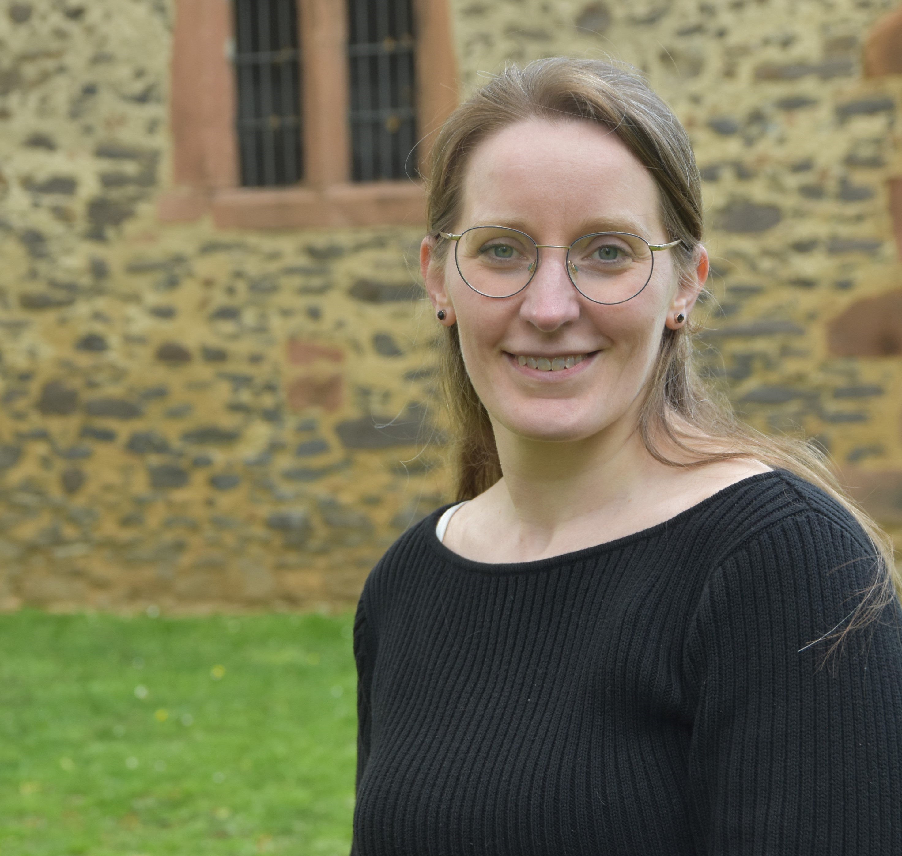Elisabeth Engler-Starck sitzt auf einer Mauer vor dem Johanniterturm in Nidda und lächelt in die Kamera.
