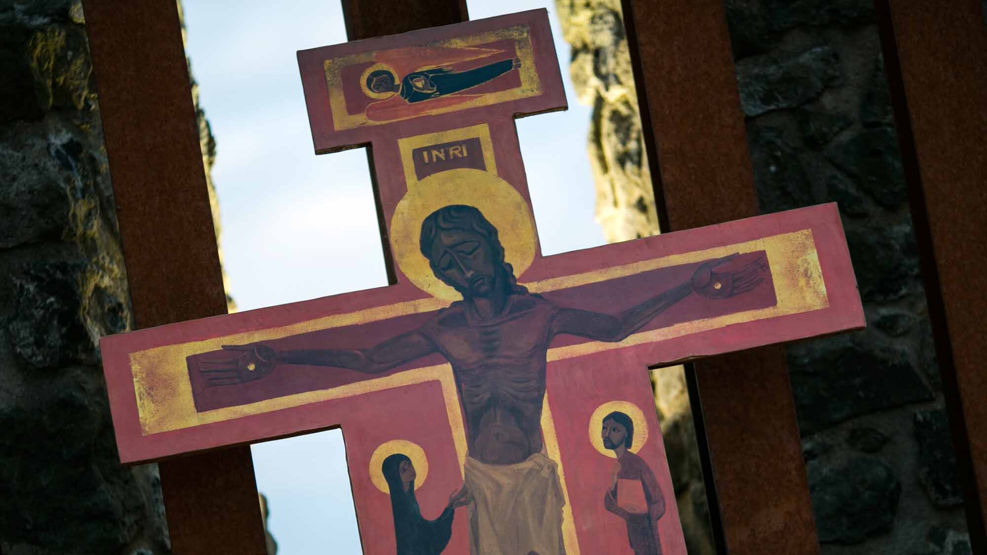 Taizé_Kreuzikone_C_Sandra Hirschke_fundus-medien.de_16zu9.jpg Kreuzikone mit dem gekreuzigten Jesus, darunter zwei Personen mit Heiligenschein, vor einer Holzkonstruktion und Felswänden.