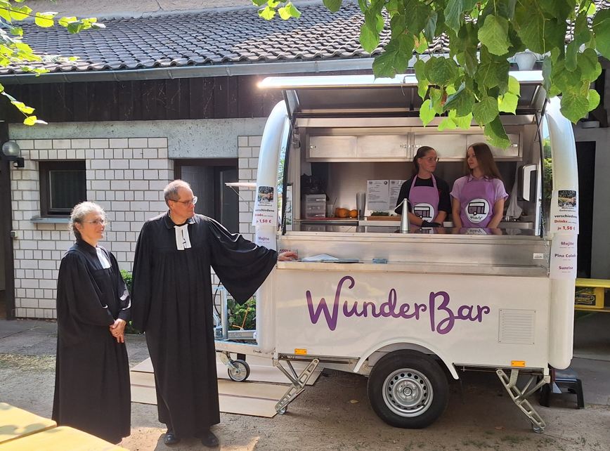 Das Bild zeigt die 2 Babenhäuser Pfarrer und eine fahrbare Bar.