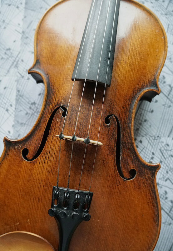 Im Bild ist der Korpus einer Violine mit Griffbrett und Saiten zu sehen. Die violine liegt auf einem Notenblatt.