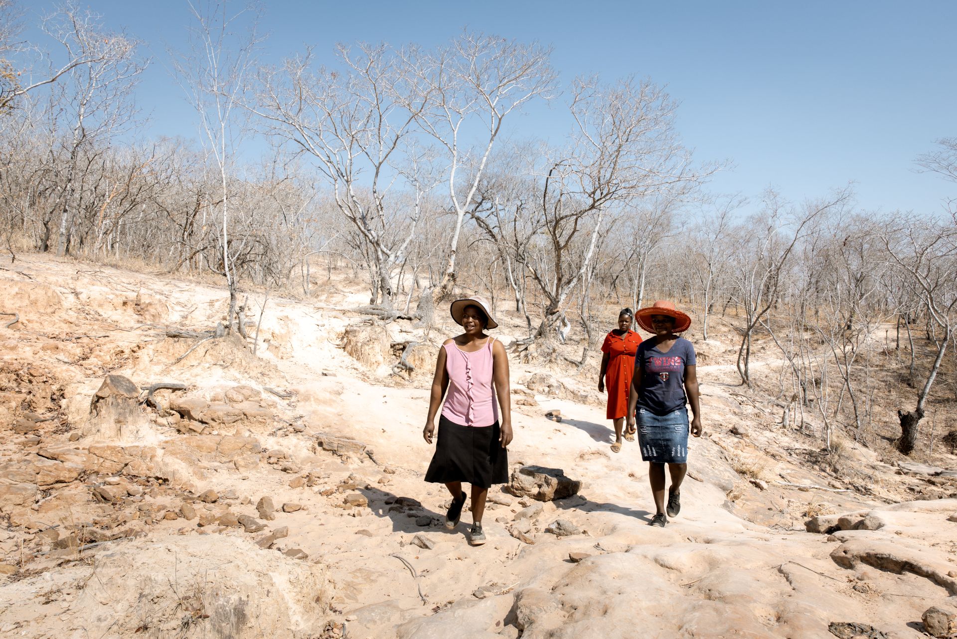 Drei Frauen gehen durch eine karge, afrikanische Landschaft.