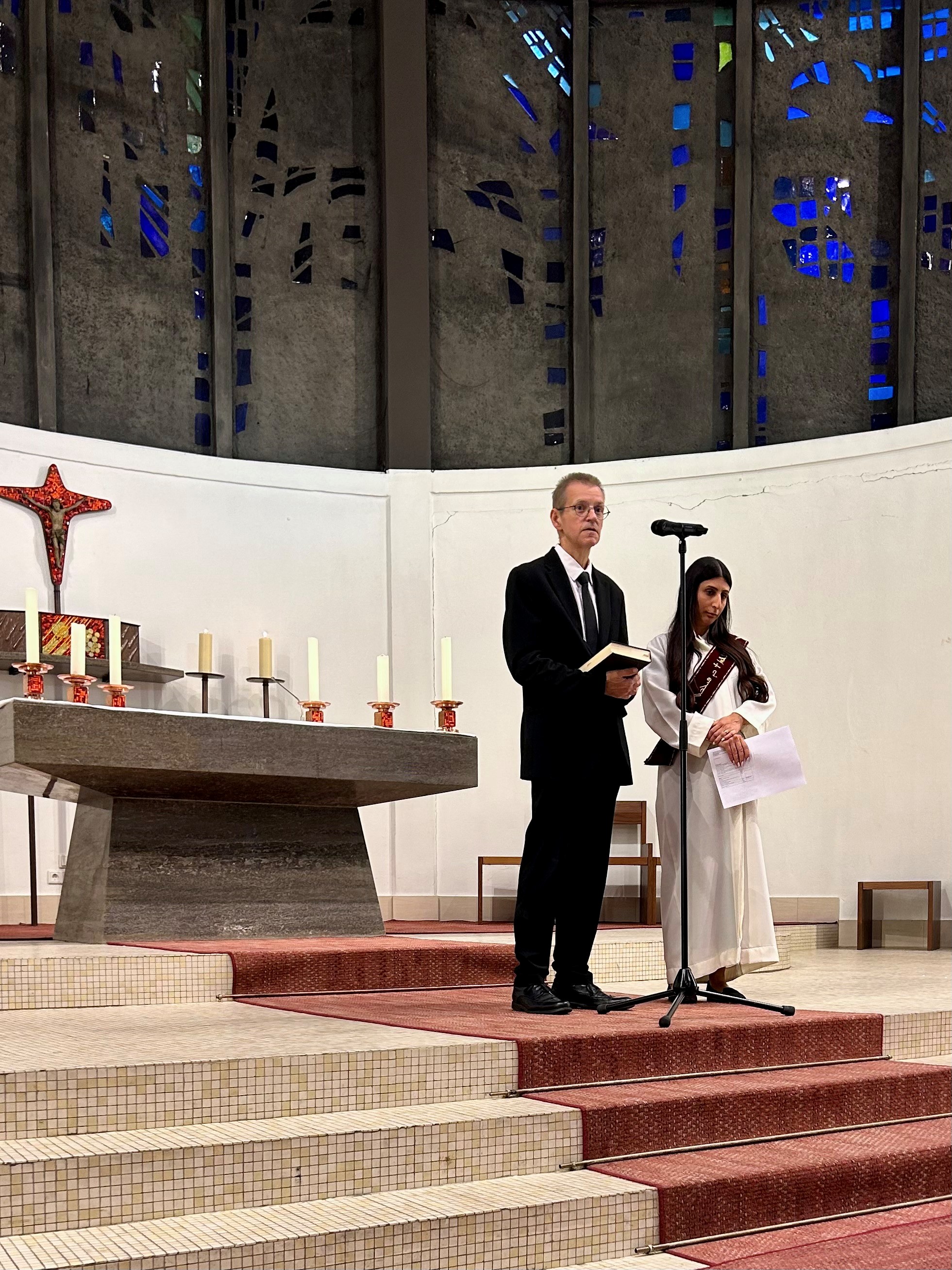 Ein Mann und eine Frau stehen in liturgischer Kleidung vor dem Altar einer Kirche.