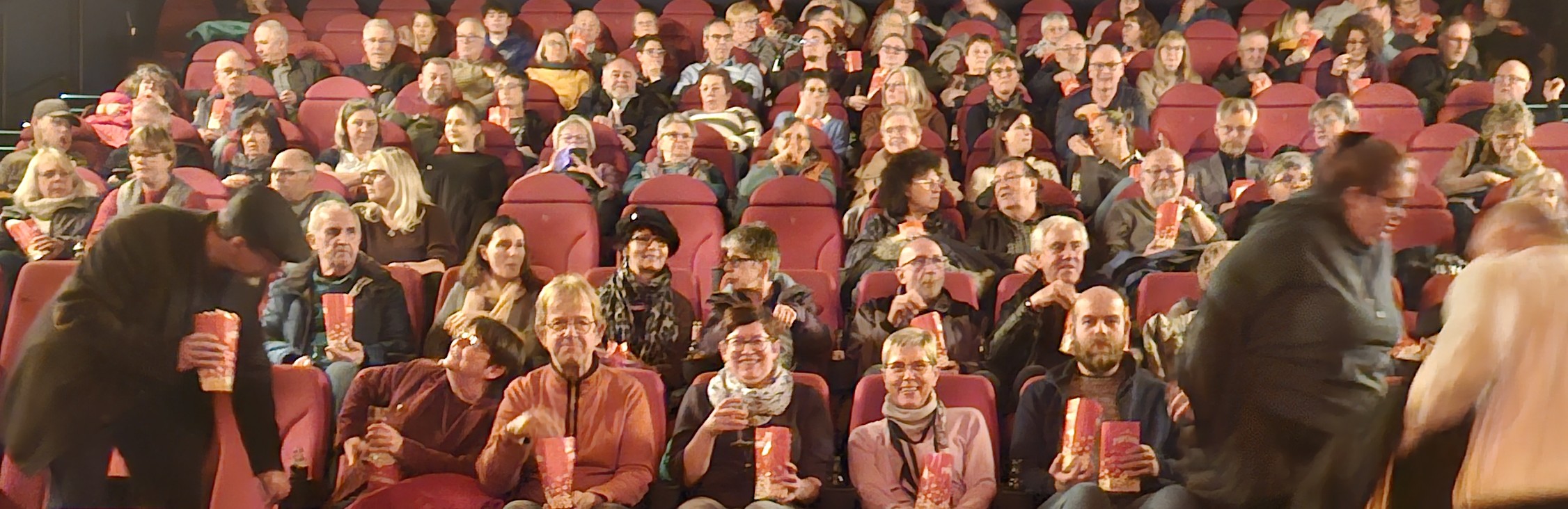 Blick in den Kinosaal: Viele gute gelaunte Menschen, manche mit einer Tüte Popcorn in der Hand, warten auf den Beginn des Films