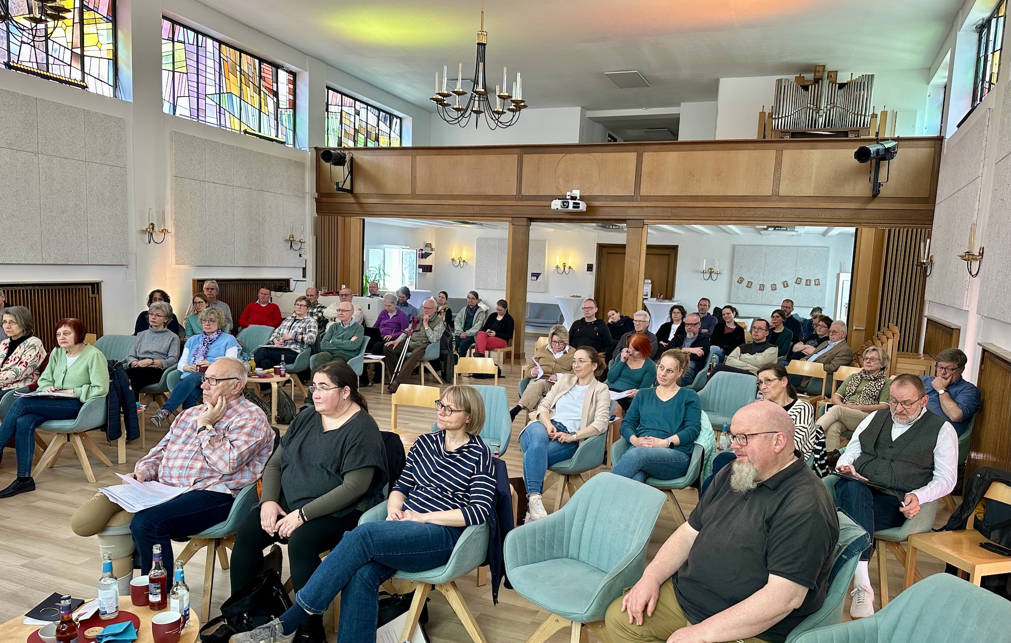 Tagung der Dekanatssynode Gruppenfoto der Teilnehmer:innen der Synodentagung des Evangelischen Dekanats Gießen in der Lukaskirche, Gießen, März 2026. Die Versammlung findet in einem hellen, freundlichen Kirchenraum mit farbenfrohen Glasfenstern und einer Orgel im Hintergrund statt. Die Teilnehmer:innen sitzen auf Stühlen in Reihen und folgen aufmerksam der Veranstaltung.