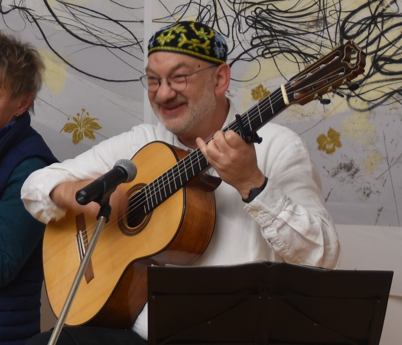 Daniel Kempin sitzt mit einer Gitarre in den Händen auf einem Barhocker im Johannitersaal und lacht ins Publikum.
