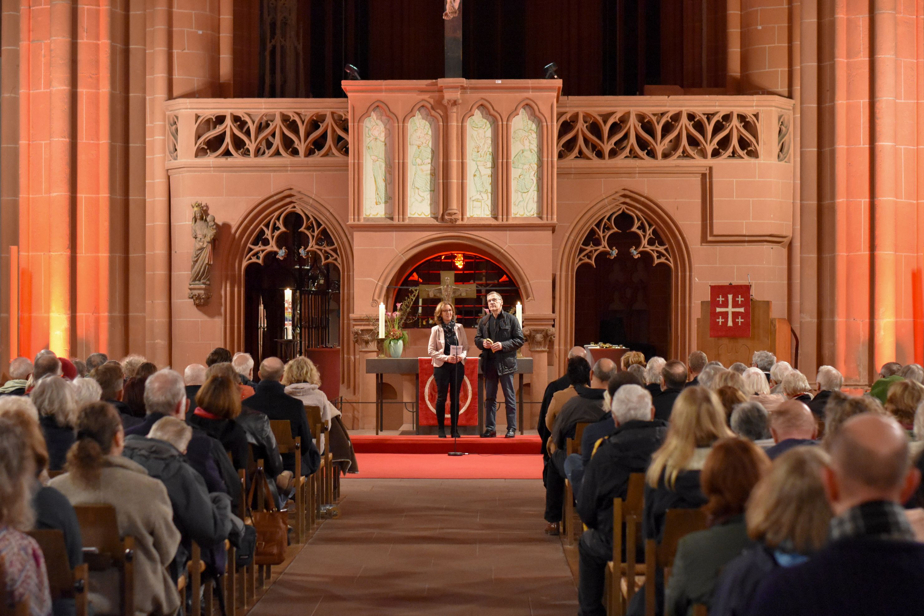 Ansicht des Innenraums einer Kirche mit Gästen, 2 Personen stehen vor dem Altar in der Mitte.