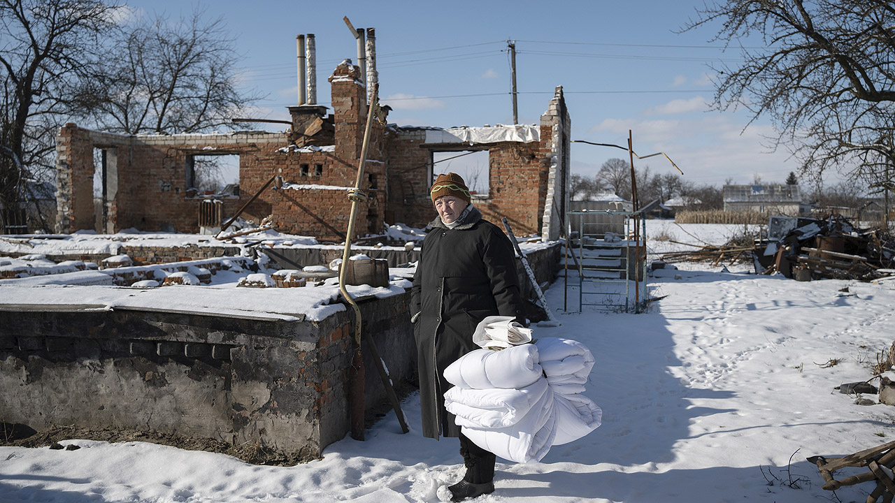 Frau mit Bettdecken vor einer Haus-Ruine
