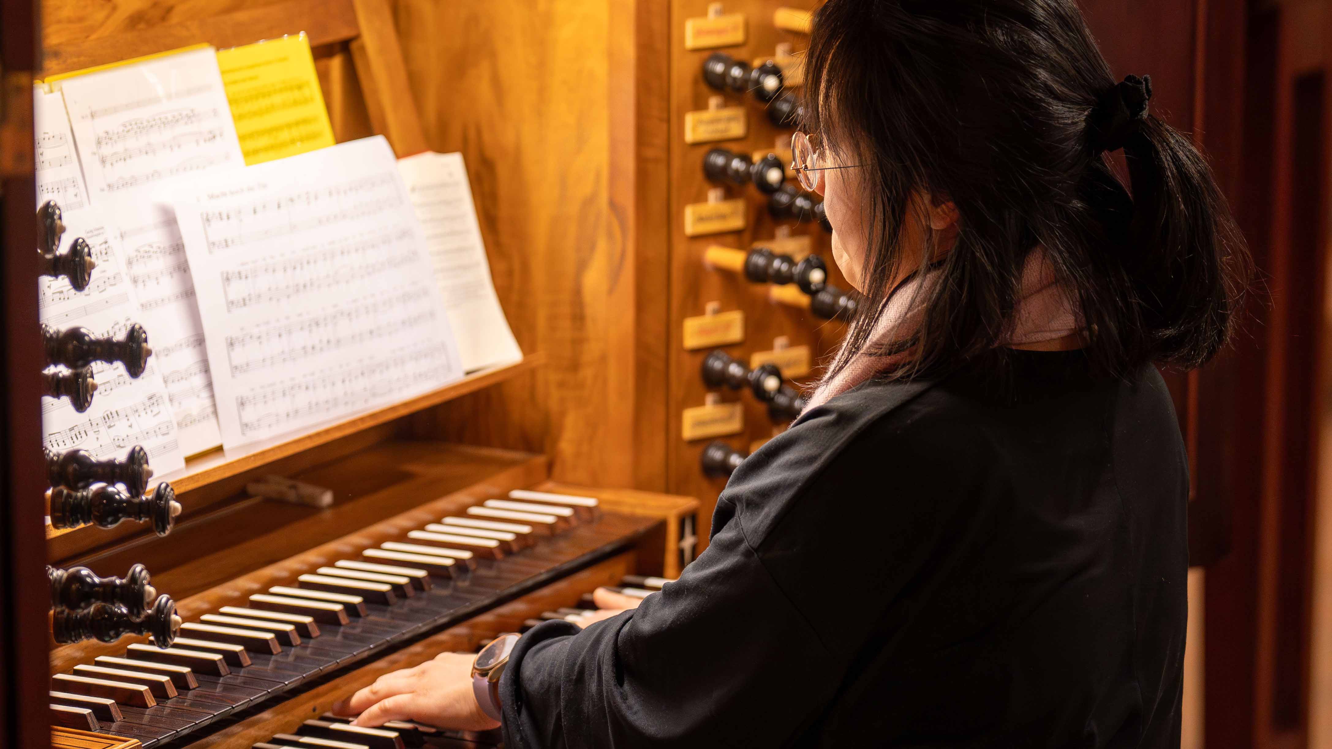 Eine Person spielt an einer Orgel mit mehreren Manualen; auf dem Notenpult stehen aufgeschlagene Notenblätter.