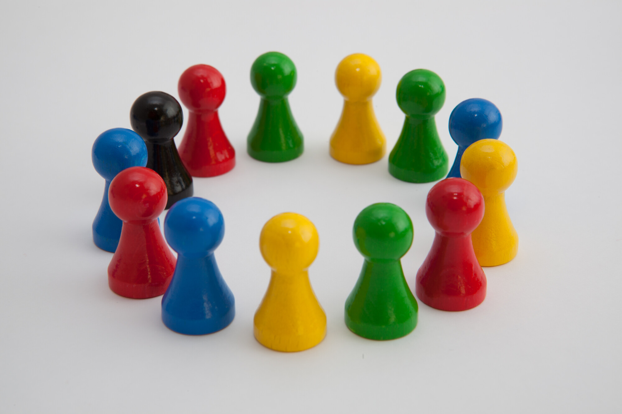 13 Spielfiguren in den Farben rot, blau, grün, gelb und schwarz stehen auf einem weißen Untergrund im Kreis