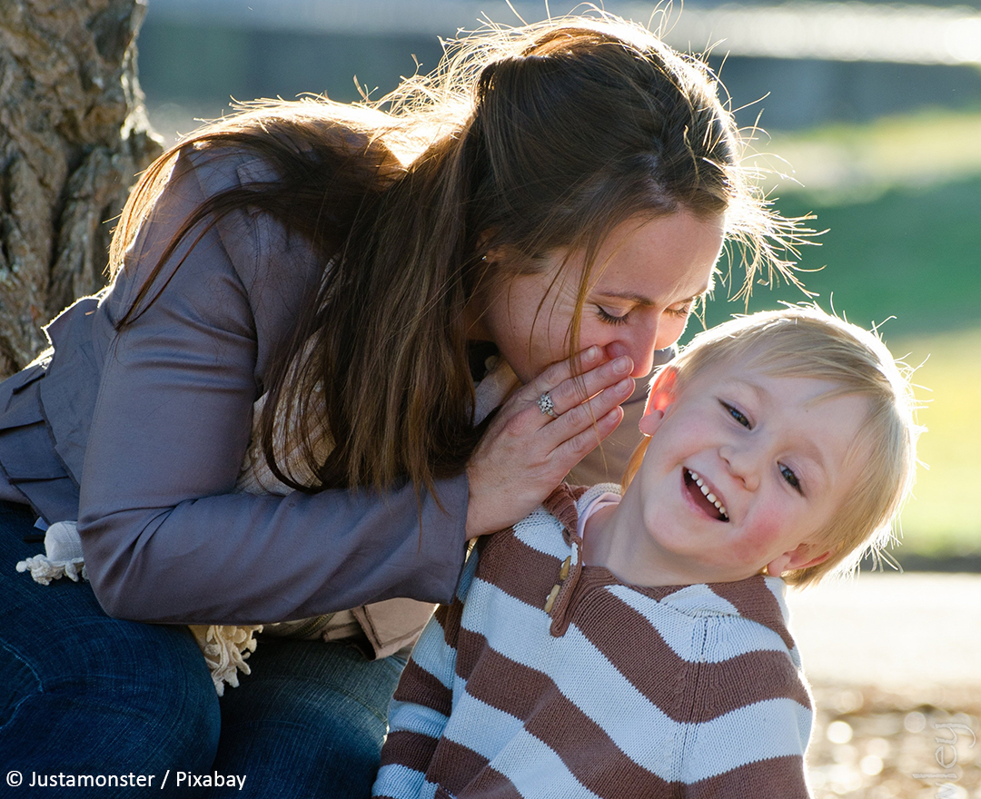 Frau flüstert Kind ins Ohr.
