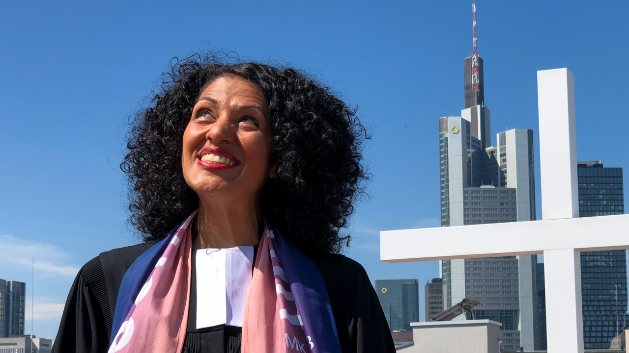 Portrait, im Hintergrund Hochhäuser in Frankfurt und ein Holzkreuz